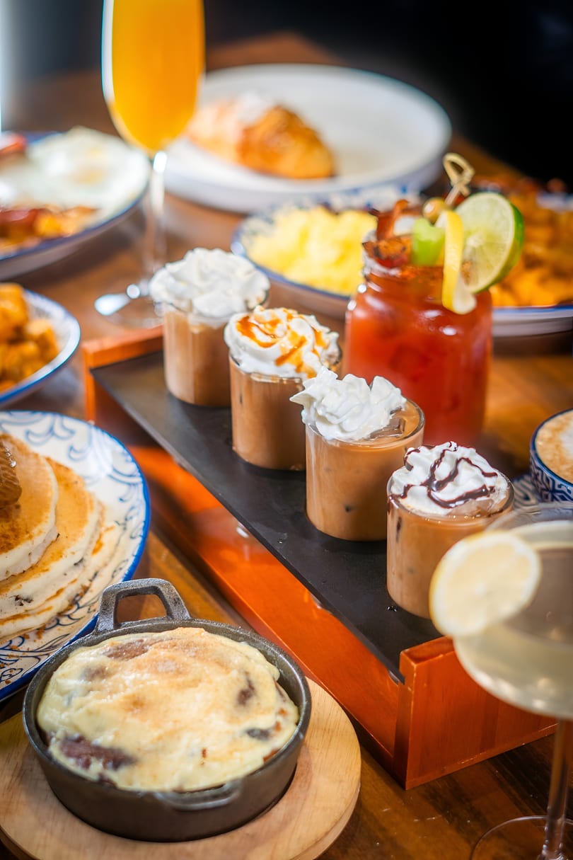 A brunch spread with iced coffees, a Bloody Mary, pancakes, and a cinnamon roll.
